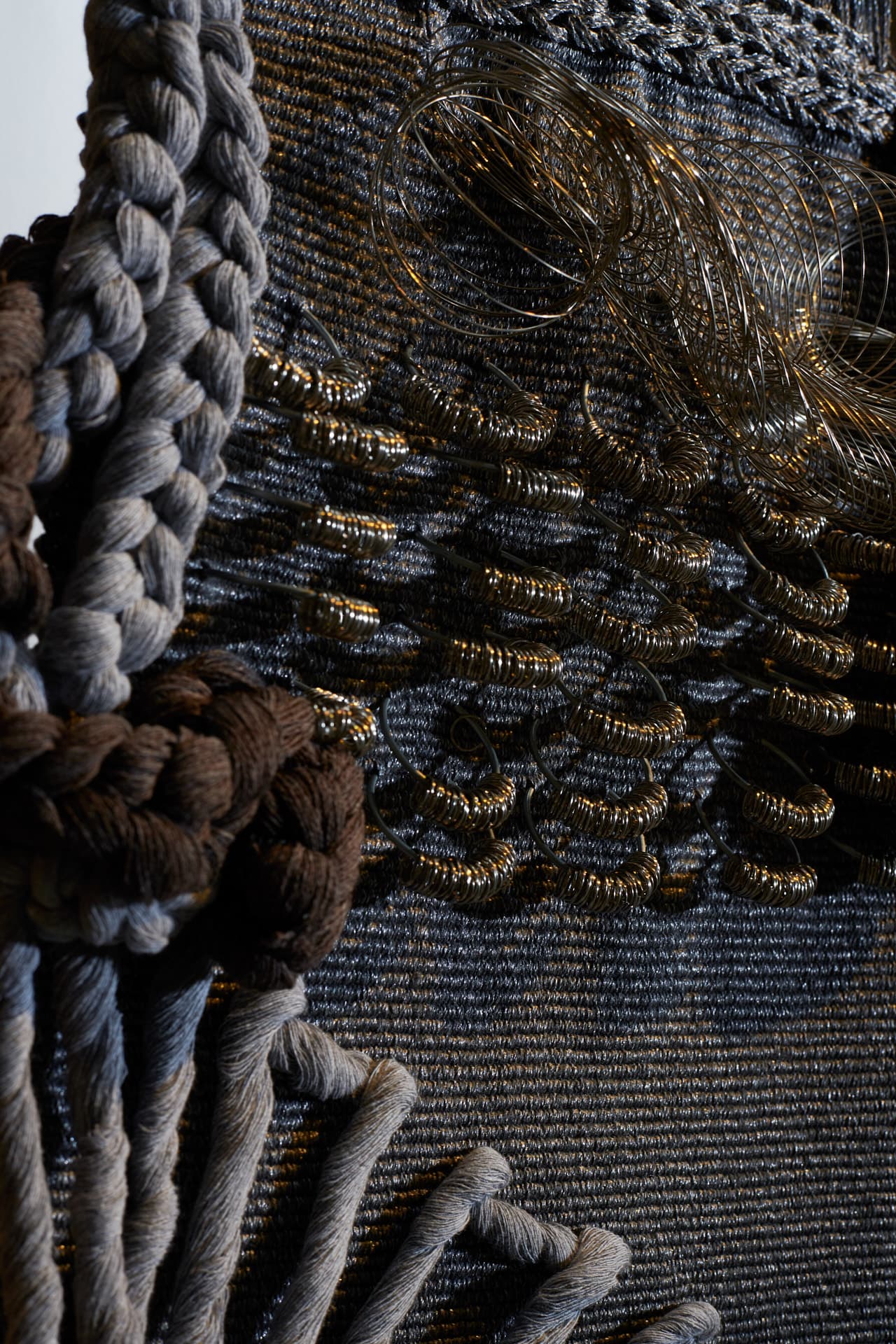 Detailaufnahme des Werks „Gestando en la fria sombra“, das aus grauen, geflochtenen Fäden und strukturierten Elementen aus Metallfäden besteht.