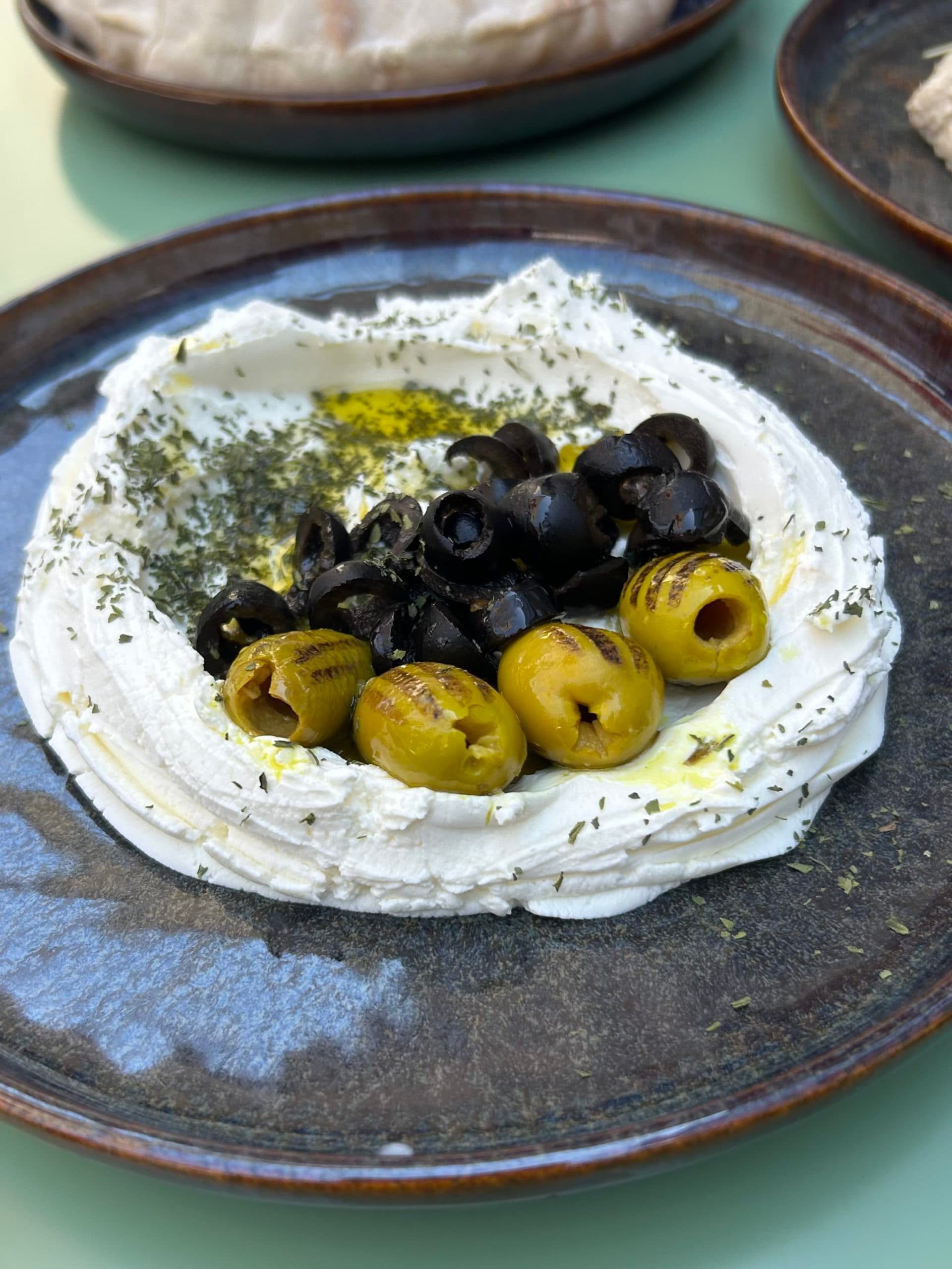 Assiette de fromage frais garni d'olives noires et vertes, avec des herbes aromatiques.