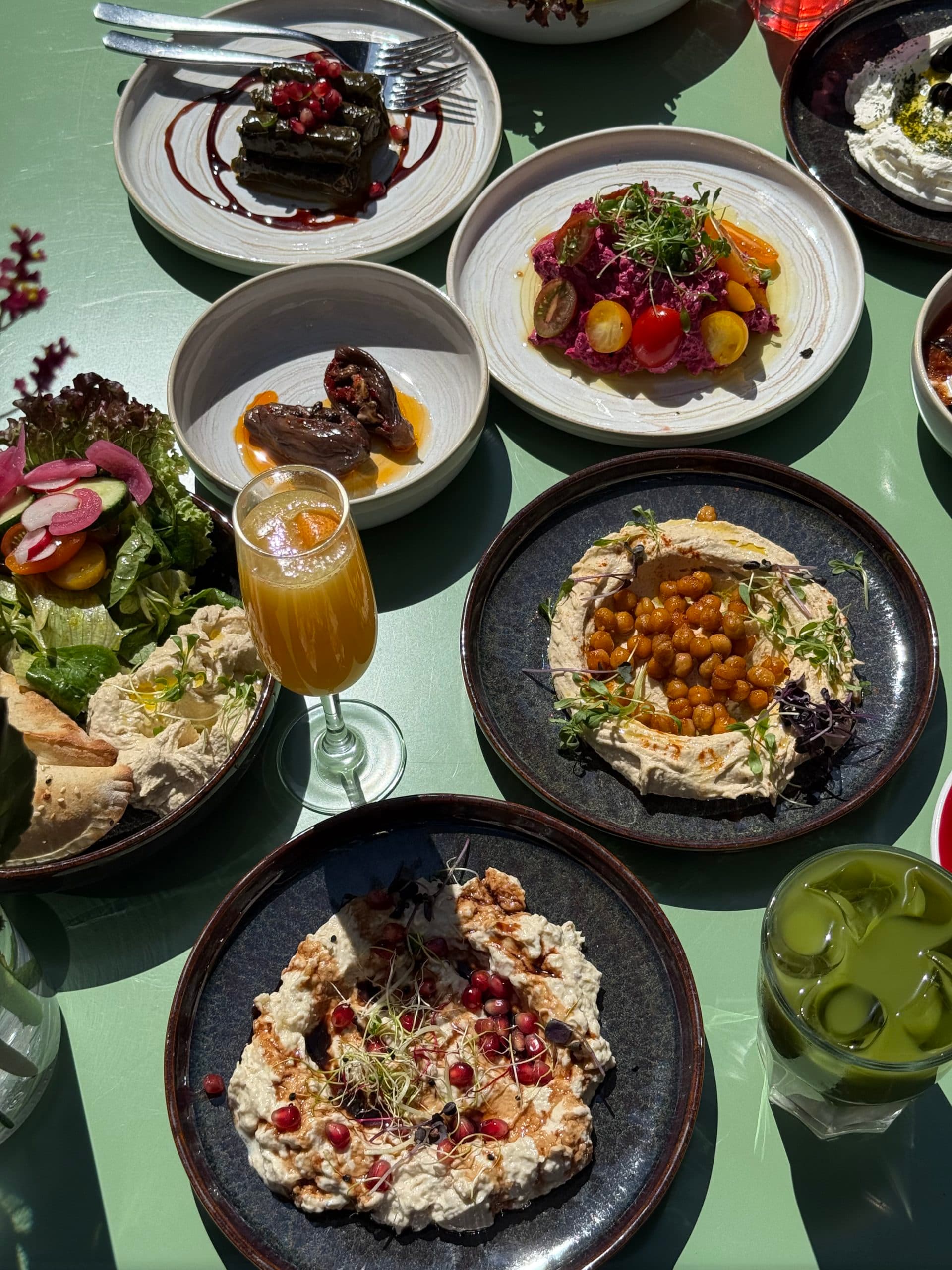 Table avec plusieurs plats à partager, boissons et assiettes de cuisine méditerranéenne.