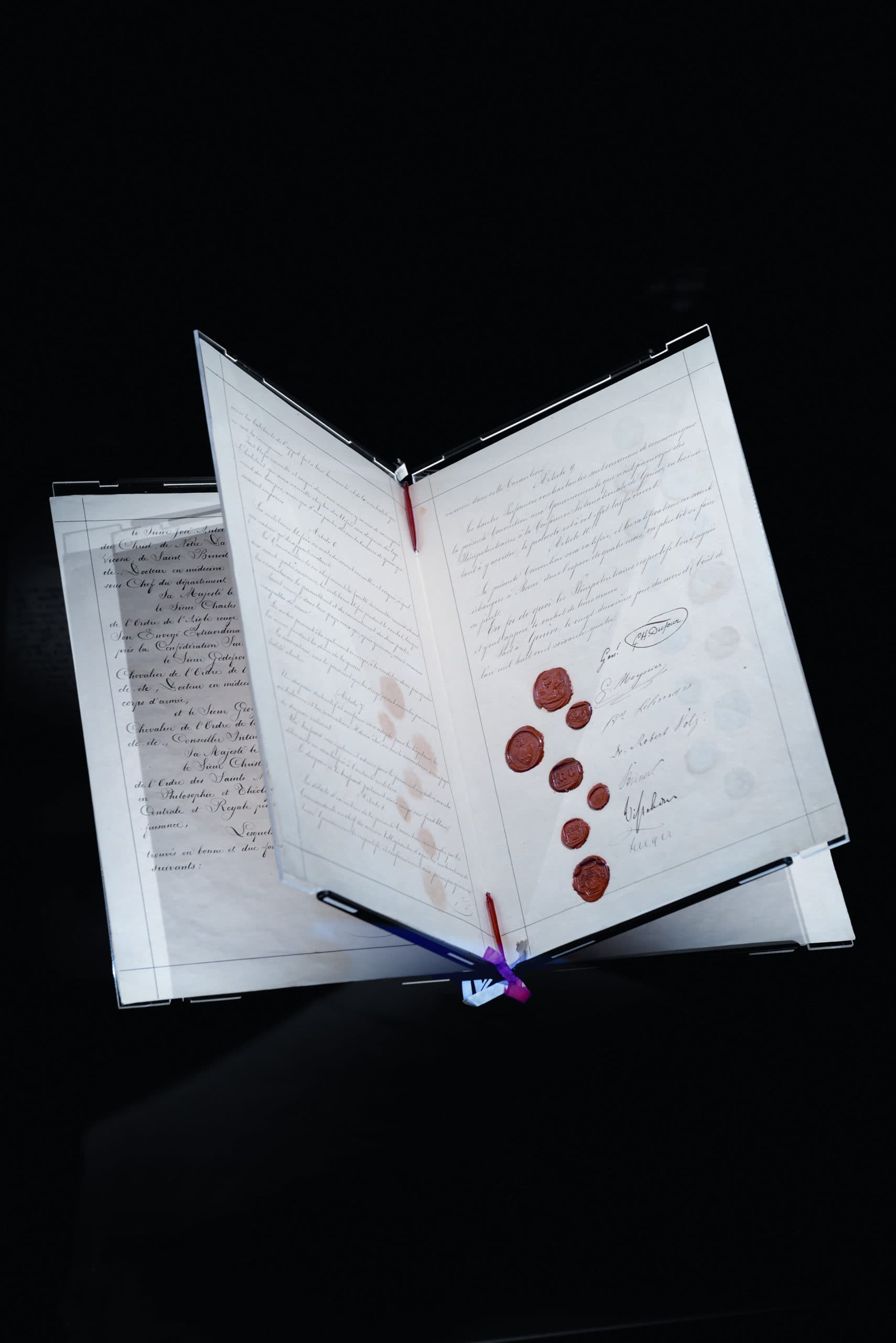Alte, fächerförmig aufgebreitete Handschriften mit Kursivschrift und roten Wachssiegeln, präsentiert vor schwarzem Hintergrund.