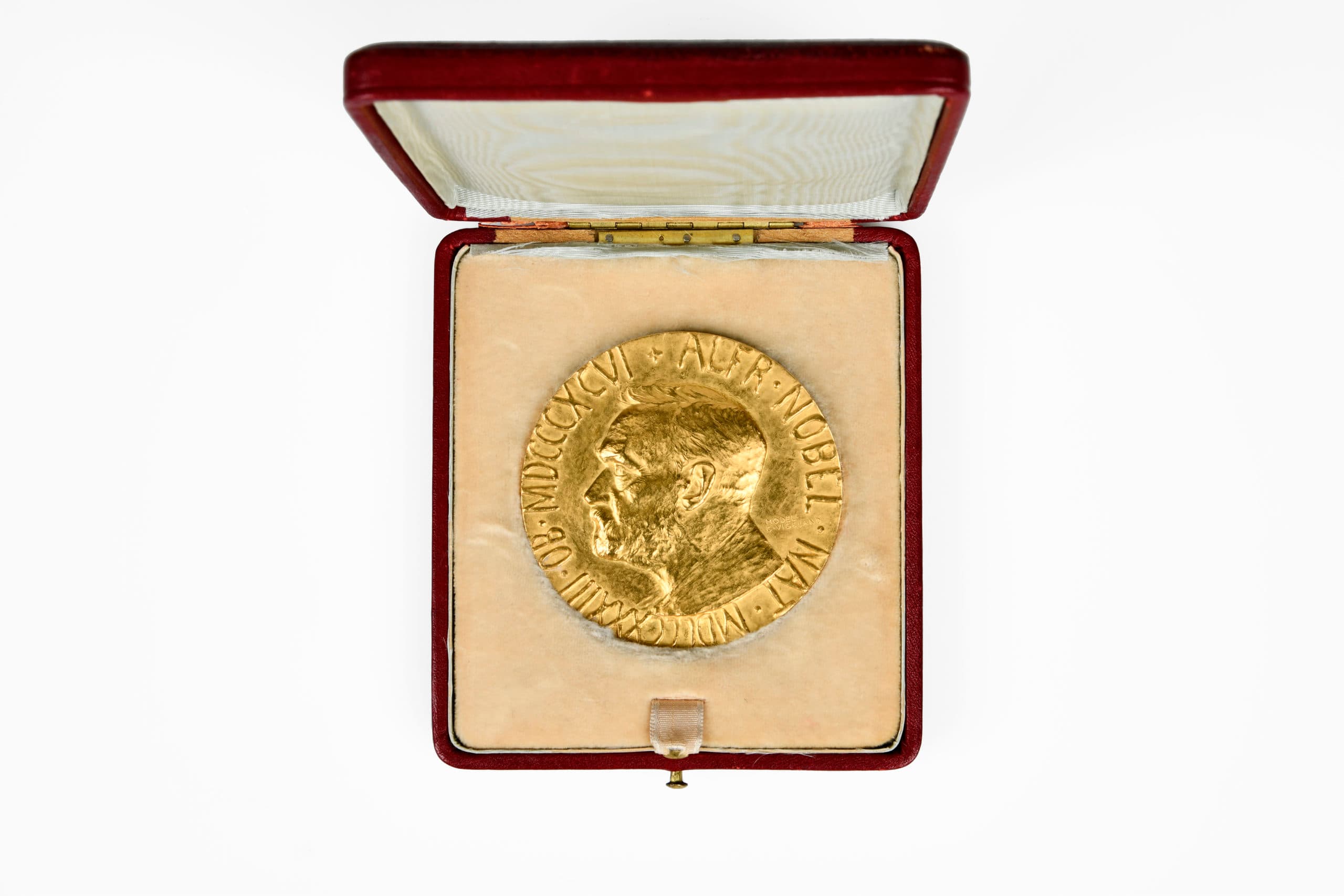 A gold medal depicting a man’s profile, presented in an open red case lined with light-coloured fabric.
