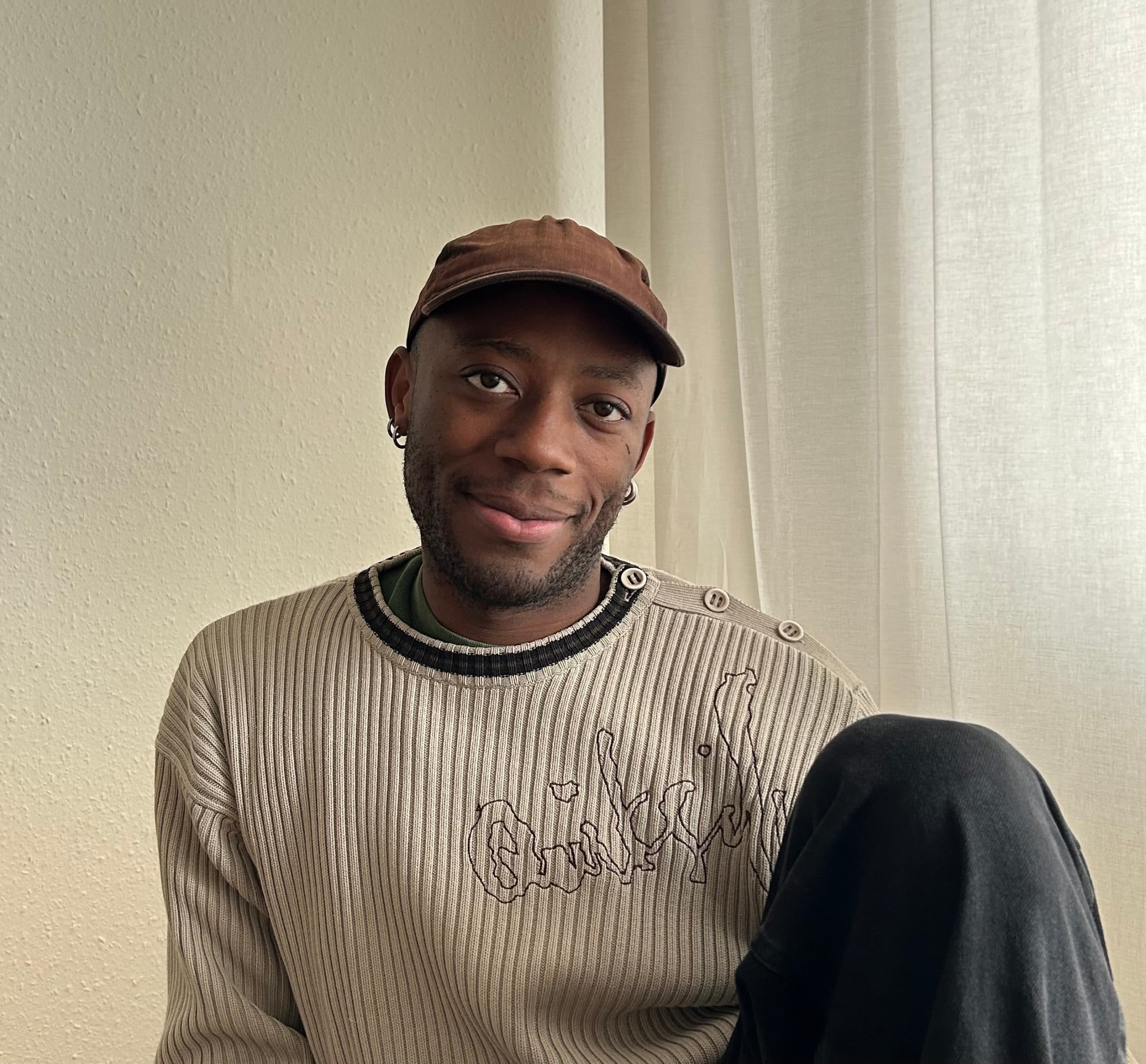 Portrait of a seated person wearing a cap and smiling slightly.