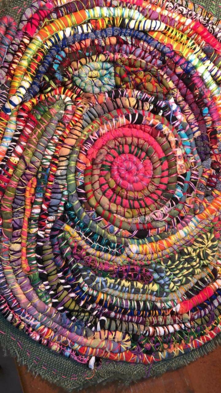Runder, mehrfarbiger Spiralteppich aus recycelten Stoffstreifen, die zusammengenäht und aufgewickelt sind.