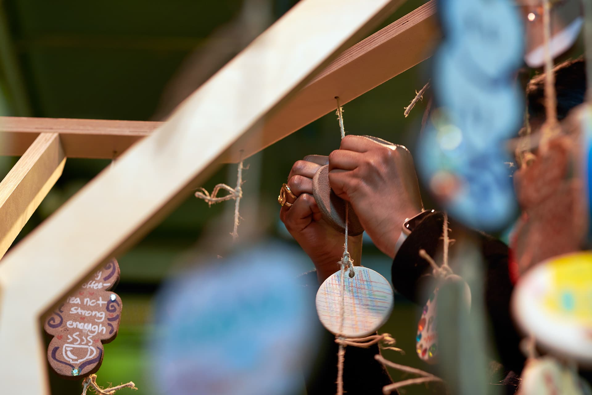 Gros plans sur des mains accrochant un un objet circulaire en céramique à une ficelle pendant d'une structure en bois.