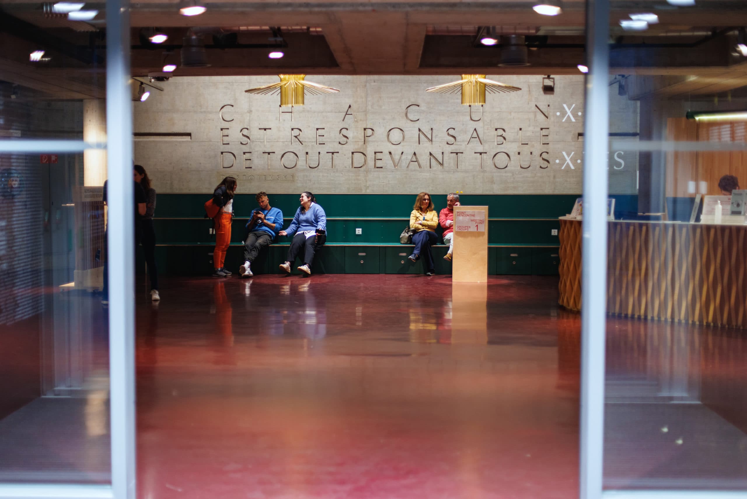 Interior reception area with a counter and several people standing or moving through a modern hall.