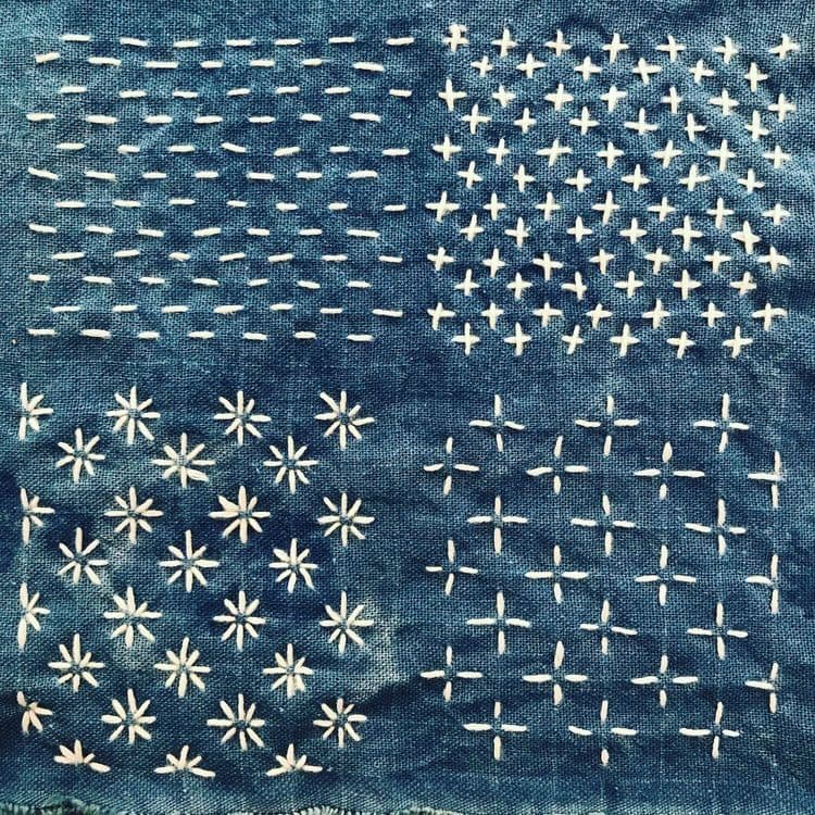 Sashiko-Stiche in Form von Kreuzen, Sternen oder Linien, die mit weißem Garn auf indigoblauem Stoff ausgeführt sind.