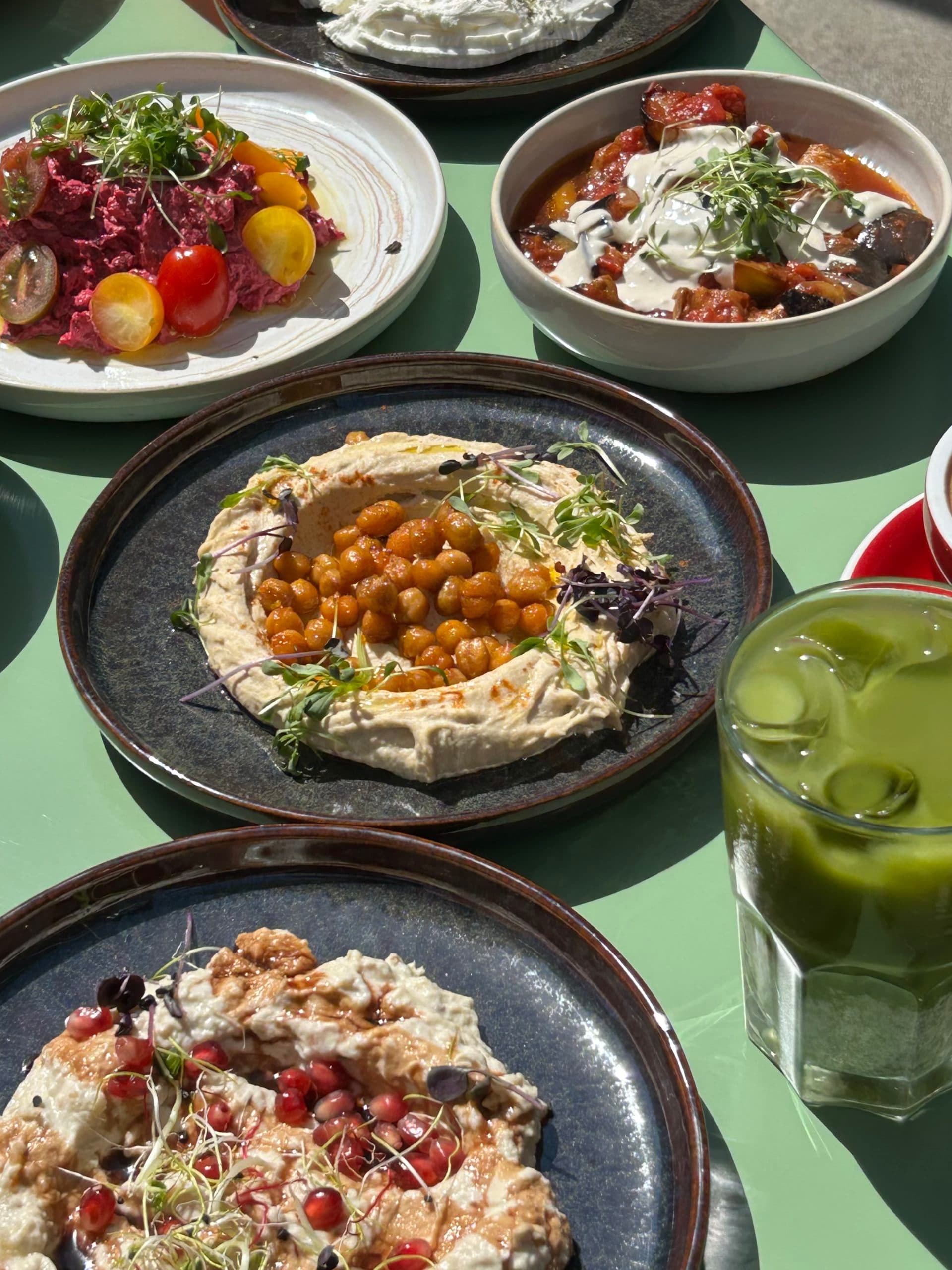 Tisch mit verschiedenen Gerichten zum Teilen, Getränken und Tellern mit mediterraner Küche.